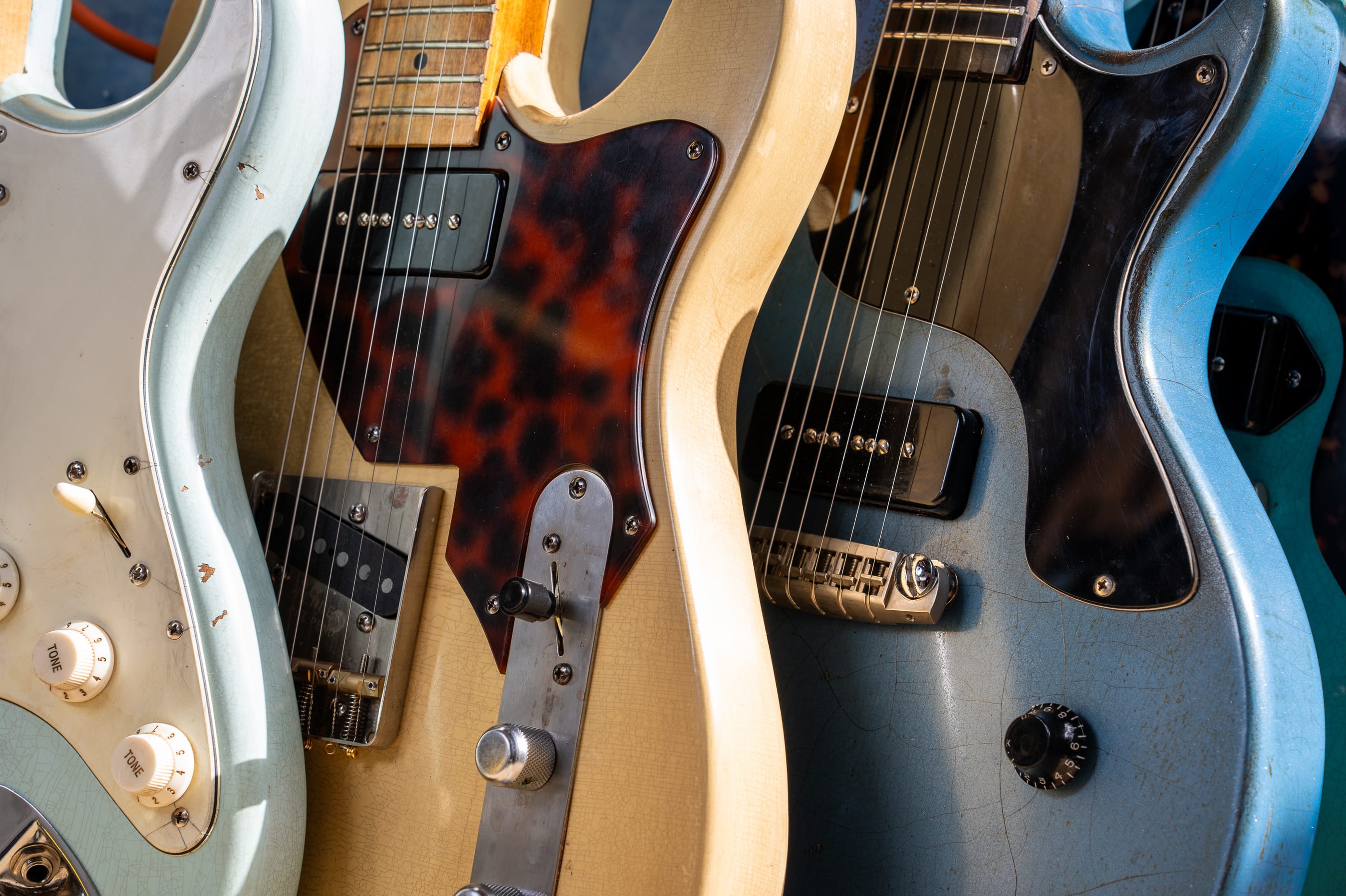 Three of his guards side by side: aged white on a sonic blue Strat, tort on a blonde Tele, black on a blue single-cut